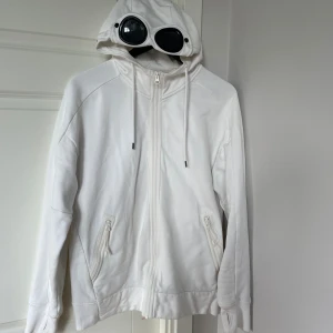 CP company hoodie  - Säljer min vita CP company hoodie då jag inte använder den längre. Hoodien är i ganska bra skick förutom ena glaset som har en liten repa/spricka. Äkthets bevis finns. Köpt för ungefär 2 år sedan. Hör gärna av er vid frågor!