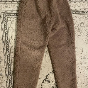 Mjuka mysbyxor i teddymaterial - Supermysiga bruna mjukisbyxor i fleece från Hunkemuller.  Byxorna har en loose passform och dragsko i midjan för extra komfort. Perfekta för chill dagar hemma eller när du vill vara extra bekväm.