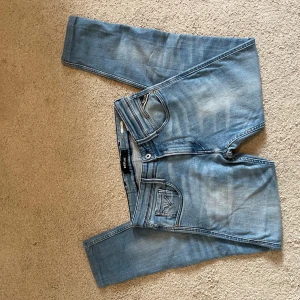 Replay Anbass ljusblå jeans - Säljer ett par Replay Anbass jeans i ljusblå tvätt med snygga slitningar. Klassisk femficksmodell med Replay-logga på bakfickan och detaljerade sömmar. Jeansen har normal passform och är tillverkade i mjukt denimtyg för en skön känsla. Storlek 29/32