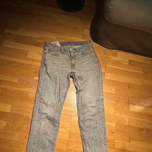 Grå Levis 511 jeans straight fit - Säljer ett par grå Levis 511 jeans med klassisk femficksdesign och raka ben. Jeansen har en snygg tvättad look och är tillverkade i mjukt jeanstyg. Lite mindre hål som jag endast tkr gör de snyggare men där av priset. L:29 W:30.