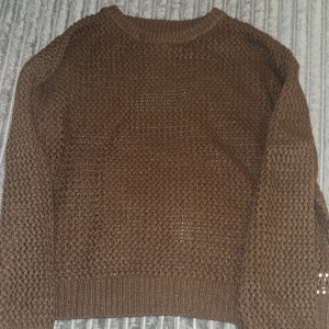 Brun stickad tröja med grov struktur - Säljer en brun stickad tröja med grov, luftig struktur och rund halsringning. Tröjan har långa ärmar och ribbade muddar vid ärmslut och nederkant. Perfekt för lager-på-lager under kyliga dagar.