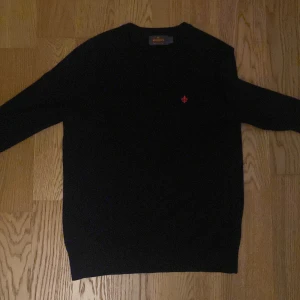 Mörkblå merinoullströja från Morris XS - Säljer en mörkblå stickad tröja från Morris i 100% merinoull. Klassisk modell med rund halsringning, lång ärm och en liten röd broderad logga på bröstet. Perfekt för dig som gillar stilrena och bekväma plagg med premiumkänsla.