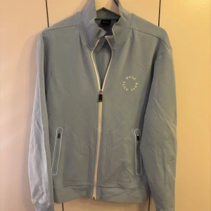 Ljusblå ziptröja från BOSS - Snygg ljusblå tröja från BOSS med hel dragkedja och ståkrage. Lite smutsig vid kragen, går säkert att få bort om man använder rätt saker! nytt pris drygt 1000