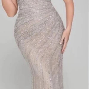 Glittrig långklänning i champagne - Supersnygg långklänning i champagnefärg med glittriga detaljer och figurnära passform. Klänningen har ett elegant mönster av glittrande pärlor och paljetter som ger en lyxig känsla. Perfekt för dig som vill sticka ut på bal eller fest.