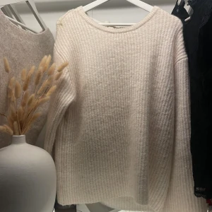 Vit stickad tröja med rosett - Supermysig vit stickad tröja med lång ärm och öppen rygg som knyts med en bred rosett. Tröjan har en ribbad struktur och en avslappnad passform, perfekt för lager på lager under kyliga dagar| skriv vid intresse💕