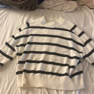 Randig stickad tröja från Amisu - Säljer en vit och svart randig stickad tröja från Amisu. Tröjan har en hög, ribbad krage och breda muddar vid ärmslut och nederkant. Oversized passform och klassiska horisontella ränder ger en chill vibe.