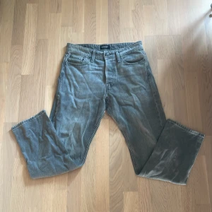 Grå jeans från Jack & Jones - Snygga grå jeans från Jack & Jones med klassisk femficksdesign och raka ben. Jeansen har en cool tvättad look och är tillverkade i mjukt denimtyg. Perfekta för dig som gillar en avslappnad och stilren vibe.