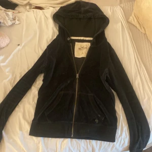Svart velour hoodie från Hollister - Mysig svart hoodie från Hollister i mjuk velour med dragkedja framtill och huva. Använd mycket, smörerna borta, lite fläckig, och kludd fastnat i luvan… 🫣 Pga dåligt skick  20 kr + 30kr frakt! 💝