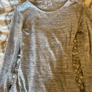 Grå långärmad tröja från H&M - En enkel och stilren grå långärmad tröja från H&M. Tröjan har en rund halsringning och är tillverkad i mjuk bomullsmix. Perfekt för lager-på-lager och passar till det mesta i garderoben.