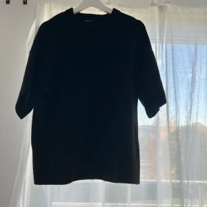 Svart stickad tröja från Gina Tricot - En svart stickad tröja från Gina Tricot med ribbad rund halsringning och halvkort ärm. Enkel och stilren modell som är lätt att matcha till olika outfits. Perfekt för lager-på-lager under höst och vinter.