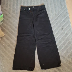 Svarta wide jeans från Gina Tricot - Svarta jeans från Gina Tricot i modellen Perfect Jeans. Byxorna har raka, vida ben och klassisk femficksdesign. Tillverkade i ett mjukt bomullstyg med dragkedja och knapp framtill. Perfekta för dig som gillar en avslappnad och trendig look.