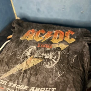 AC/DC svart vintage t-shirt S - Svart t-shirt med coolt vintage AC/DC-tryck framtill, inspirerat av bandets klassiska album. T-shirten har korta ärmar, rund hals och ett slitet, tvättat utseende. Materialet är mjuk bomull som känns skönt mot huden. Perfekt för dig som älskar rock och vill sticka ut.