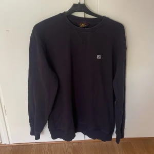 Mörkblå sweatshirt från Lee, storlek L - En mörkblå sweatshirt från Lee i regular fit med rund hals och diskret Lee-logga på bröstet. Tröjan har långa ärmar, ribbade muddar och är tillverkad i mjukt material som passar perfekt för en chill och stilren look. Jätte bra skick, inte använd mycke eftersom den blev för lite för fort, skulle säga liten L