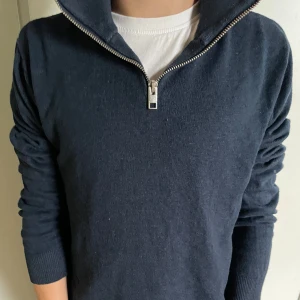 Mörkblå half zip tröja Jack & Jones - Mörkblå stickad tröja från Jack & Jones med half zip-dragkedja och hög krage. Tröjan har lång ärm och ribbade muddar, perfekt för lager-på-lager. Enkel och stilren design som funkar till det mesta.