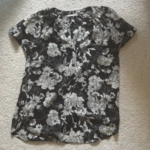 Svart blommig blus från H&M - Säljer en svart blus från H&M i storlek 36 med vitt blommönster. Blusen har korta ärmar, v-ringning och är tillverkad i ett lätt och mjukt material som känns skönt mot huden. Perfekt för dig som gillar en stilren men ändå cool look.