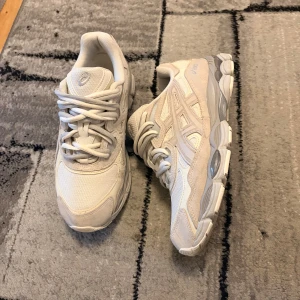 Vita ASICS GEL sneakers (sällsynt) - Säljer ett par fräscha vita ASICS GEL sneakers med snygga detaljer i mesh och mocka. Skorna har en chunky sula, klassisk snörning och diskreta silverinslag på sidorna. Perfekta för dig som gillar sportig och clean stil. Ett par snygga Asics med grå och krämvit snörre.  Köpta från JD e-kvitto finns. Äkta  Storlek 43 Mycket bra skick, knappt använda