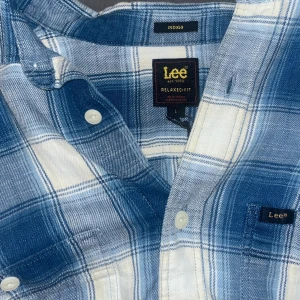 Blåvit rutig skjorta från Lee - Säljer en blåvit rutig skjorta från Lee i relaxed fit. Skjortan har klassisk krage, bröstficka med Lee-logga och vita knappar framtill. Tillverkad i mjuk bomull, perfekt för en chill och avslappnad stil.