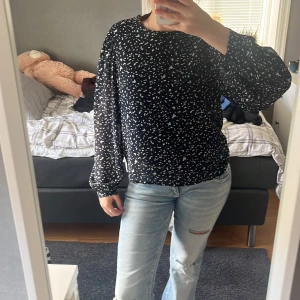 Svart blus med vita prickar - Säljer en svart blus med vita prickar och ballongärmar. Blusen är i ett lätt och luftigt material, har rund halsringning och långa ärmar med breda muddar. Perfekt att styla med jeans för en chill men snygg look.