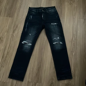 Svarta slitna jeans Alessandro Zavetti - Snygga svarta jeans från Alessandro Zavetti med slitningar och trasiga detaljer på benen. Jeansen har fem fickor, raka ben och en cool tvättad look. Perfekta för dig som gillar streetstyle och vill ha ett par jeans med attityd.