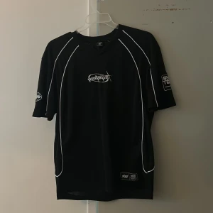 Svart sportig t-shirt Chaotic System - Svart t-shirt från Chaotic System med vita kontrastsömmar och tryck på bröstet, ärmarna och ryggen. Stort nummer 38 på ryggen och coola logodetaljer. Tillverkad i lätt polyester, perfekt för sport eller streetwear.