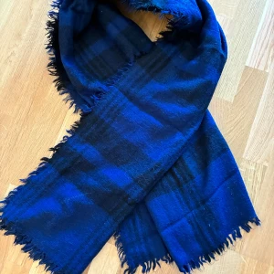 Blå och svart rutig halsduk Gina Tricot - Halsduk från Gina Tricot i blått och svart rutigt mönster. Halsduken har fransade kanter och är tillverkad i 100% akryl. Perfekt att svepa runt sig när det är kallt ute. Från djur-rök och parfymfritt hem.