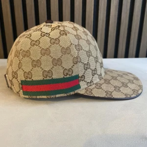 keps med GG-mönster - Kan gå ner i pris om man följer mig och likar andra av mina plagg!!       Snygg keps i beige och brunt med klassiskt GG-monogram över hela kepsen. På sidan finns den ikoniska gröna och röda randen. Kepsen är tillverkad i canvasliknande material och har böjd skärm. Perfekt för någon som vill ha en fin och snygg huvudbonad.