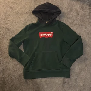 Mörkgrön Levi's hoodie med logga - Säljer en mörkgrön hoodie från Levi's med klassisk röd logga på bröstet. Tröjan har mörk blå huva, magficka och långa ärmar. Den har för det mesta legat i garderoben ganska länge så vill egentligen ba bli av med den. Hoodie e i lite ”tjockare” material, skulle inte säga att den e en tun hoodie. Inga defekter 