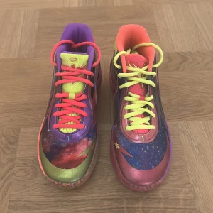 Puma MB.01 Galaxy sneakers - Färgstarka Puma MB.01 Galaxy sneakers i syntetmaterial med galaktiskt mönster, mix av lila, rosa, blått, gult och grönt. Skorna har snörning, platt sula och coola detaljer som texten 'RARE' under sulan och 'MELO' på hälen. Perfekta för dig som vill sticka ut.