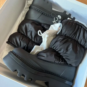 Svarta moon boots från Chloé - Chunky svarta moon boots från Chloé med grov sula och vadderad nylon upptill. Skorna har dragsko upptill, rund tå och Chloé-logga bak samt coolt märke framtill. Perfekta för vintern och riktigt statement med sin pösiga design. Helt nya.