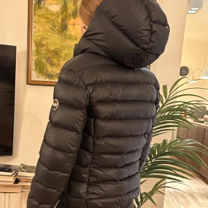 Svart Colmar dunjacka med huva  (XS) - Svart dunjacka från Colmar med huva och dragkedja. Jackan är quiltad och har en klassisk pufferstil med diskret logga på ärmen. Perfekt för kalla dagar! (En av bilderna är lånad). 