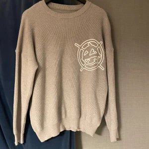 Grå stickad Vicinty tröja  M - Grå stickad Vicinity tröja i medium med coolt vitt tryck på bröstet. Tröjan har rund hals, ribbade muddar och är tillverkad i en mjuk blandning av core yarn och akryl. Perfekt för dig som gillar stilrena plagg med en twist.