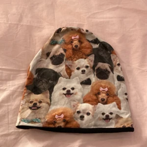 Fleecemössa med hundmotiv från Be Kind - Söt och färgglad mössa med tryck av olika hundraser, vissa med rosetter och flugor. Utsidan är i mjuk bomull och insidan fodrad med svart fleece för extra värme. Märkt med Be Kind-lapp. Perfekt för dig som älskar hundar 🐶 💖💖💖 Är faktiskt egengjord och då extra bra kvalitet 🥰🐶💞