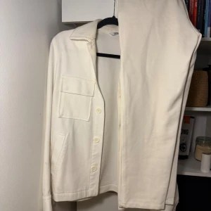 Vit kavaj och byxa från Zara - Säljer en stilren vit kostym från Zara med kavaj och matchande byxa. Kavajen har klassisk krage, bröstficka med lock, knäppning framtill och raka ärmar. Byxan är enkel och rak i modellen. Perfekt för dig som gillar minimalistisk stil.