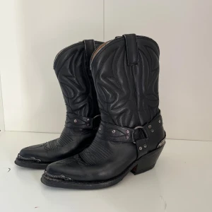 Svarta cowboy boots med döskalle-detalj - Riktigt feta svarta cowboy boots i skinn med coola silvriga döskalle-detaljer på hälen. Perfekt edgy westernstil.