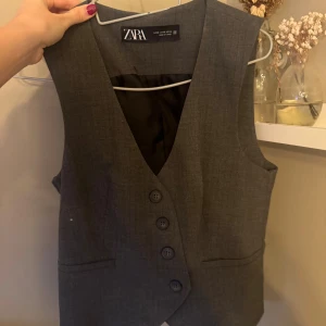 Grå väst från Zara med knappar - Snygg grå väst från Zara med klassisk v-ringning och fyra knappar framtill!🩶Skriv för fler bilder på! Endast använd en gång! Den är i XS men upplever den stor i storleken!