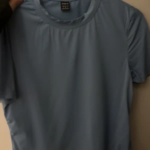 Blå t-shirt från SHEIN - Enkel blå t-shirt från SHEIN med rund halsringning och korta ärmar. T-shirten har en clean look utan mönster eller tryck och är tillverkad i ett mjukt, lätt material som känns skönt mot huden.