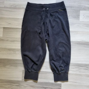 Svarta mjukisbyxor 3/4 från Vero Moda M - Svarta mjukisbyxor 3/4 från Vero Moda med resår och snörning i midjan, mudd vid benslut och en bakficka. Byxorna är i mjukt material och har en avslappnad passform, perfekta för chill dagar. Metallbricka med logga framtill, som dock har lossnat på en sidan men går att fixa.