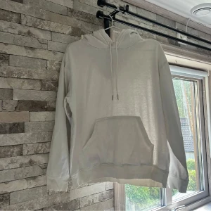 Vit hoodie från H&M med ficka - Säljer en stilren vit hoodie från H&M i storlek S. Tröjan har huva med snörning och en stor magficka framtill. Perfekt för dig som gillar en enkel och clean look. Materialet är mjukt och skönt, troligtvis bomullsmix.