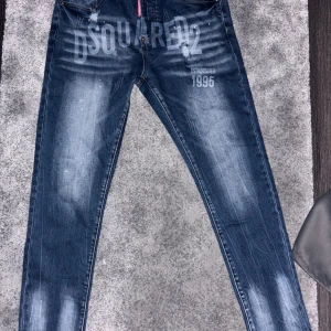 Dsquared2 blå jeans med tryck, strl 48 - Snygga blå jeans från Dsquared2 i modell Skater Jean, med stort DSQUARED2-tryck framtill och flera logotyper baktill. Jeansen har en tvättad look med ljusa partier och klassisk femficksdesign. Perfekta för dig som gillar streetwear och vill sticka ut.