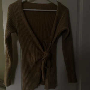 Beige ribbad omlottkofta - Säljer en beige ribbad omlottkofta med knyt i midjan. Koftan gör så man får en jätte fin figur.