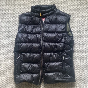 Svart dunväst från Parajumpers - Svart dunväst från Parajumpers, modell Sheen. Riktig varm och skön väst som tyvärr blivit för liten för mig, storlek Y-M skulle säga runt S. Använt skick med två stycken små lagningar se på bilden.