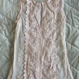 Beige spetsblus med broderi - Supersöt beige blus i transparent mesh med vackra broderade detaljer och spets längs kanterna. Ärmlös modell med romantisk känsla och fina mönster framtill. Perfekt för dig som gillar en feminin och bohemisk stil. Vet inte vart den är ifrån🩷