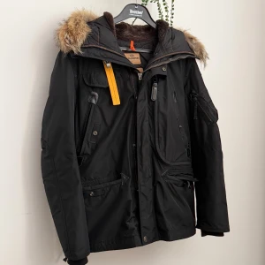 Svart Parajumpers vinterjacka med päls - Grym svart vinterjacka från Parajumpers med stor huva och snygg pälsdetalj. Jackan har flera fickor, dragkedja och coola detaljer som gul rem och patch på ärmen. Perfekt för kalla dagar och riktigt stilren look. Äkthetsbevis finns! Mycket bra skick! Mer bilder finns privat! Avtagbar päls!
