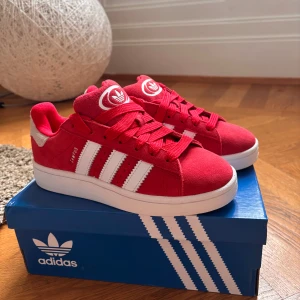 Adidas Campus 00s J röda sneakers - Riktigt snygga Adidas Campus 00s sneakers i rött mocka med klassiska vita ränder. Perfekta nu till hösten och vintern med en retrovibe och cool streetstil. Aldrig använda endast testade. Säljer pga av fel storlek. Nypris: 1099kr (Pris kan diskuteras) 💞