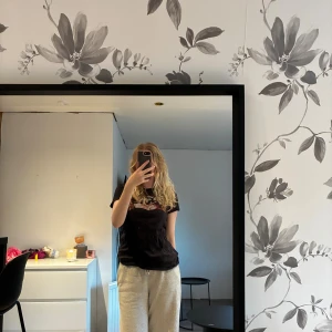 Levi's t-shirt - Svart t-shirt från Levi's med klassiskt logotryck framtill, där bakgrunden är fylld med blommigt mönster i rosa och beige toner. T-shirten har rund hals och korta ärmar. Perfekt för dig som gillar streetstyle och vill sticka ut lite extra. Knappt använd!