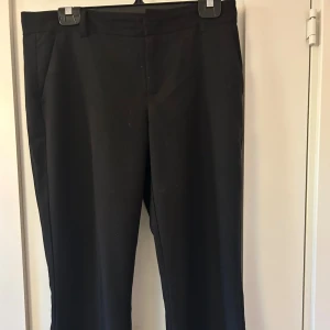 Svarta kostymbyxor med raka ben - Stilrena svarta kostymbyxor med klassisk passform och raka ben. Byxorna har hällor för bälte och diskreta sidfickor. Perfekta för en clean och dressad look. Lågmidjade
