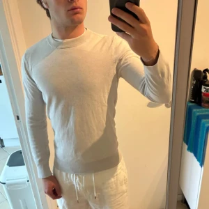 Ljusgrå stickad tröja från H&M - En stilren ljusgrå stickad tröja från H&M med rund halsringning och ribbade muddar. Tröjan har en normal passform och är långärmad, perfekt för lager-på-lager under höst och vår. Enkel att matcha med både jeans och chinos.