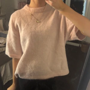 Ljusrosa stickad tröja från gina - Supermjuk ljusrosa stickad tröja med korta ärmar och ribbade kanter vid halsringning och nederkant. Perfekt för lager-på-lager och ger en chill men söt vibe till din outfit.