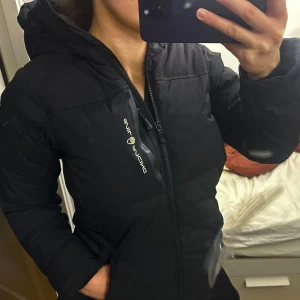 Svart dunjacka från Didriksons - Säljer en svart vinterjacka från sail racing med huva och dragkedja framtill. Perfekt för kalla dagar och riktigt skön att bära. I dam modell storlek 36