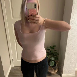 Ljusrosa topp från Gina Tricot - Säljer en ljusrosa topp från Gina Tricot med fyrkantig ringning och ärmlös design. Toppen är croppad och har en slim passform som sitter snyggt mot kroppen. Perfekt att styla med jeans eller kjol för en fräsch look.